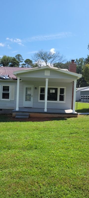 A small, white house with a porch and green lawn under a blue sky.