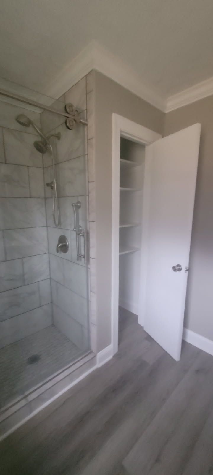 Bathroom with a tiled shower, glass door, and white open closet next to it.