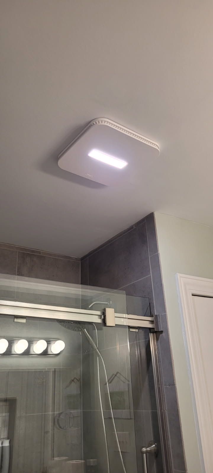 Bathroom ceiling with a recessed light fixture above a shower. Tile wall, glass door, and white trim are visible.
