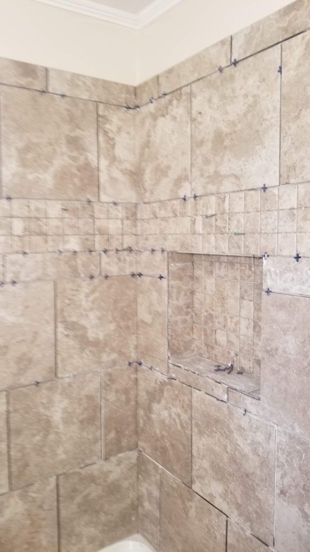 Tiled shower walls with a built-in shelf. Beige tiles are installed with visible spacers.