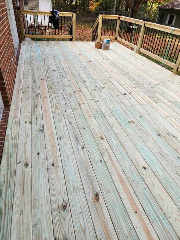 Wooden deck with railing. Light-colored planks extend from brick building towards backyard.
