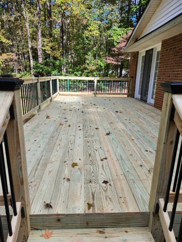 Newly constructed wooden deck with railings, leaves on the boards, and a brick house in the background.