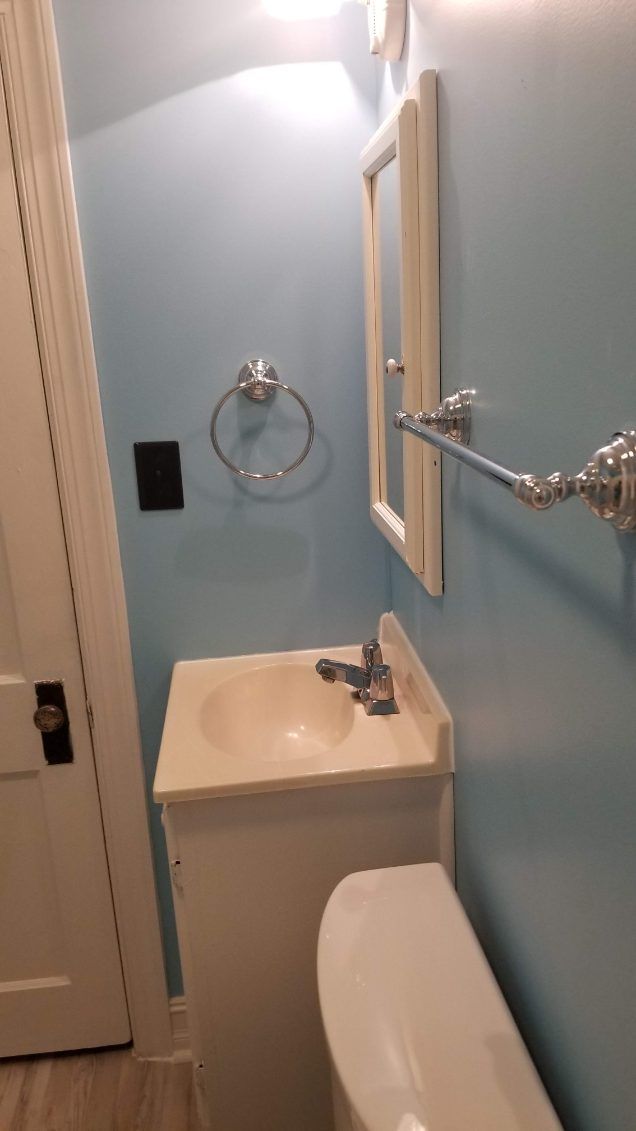 Small bathroom with a white sink, toilet, mirror, and blue walls.