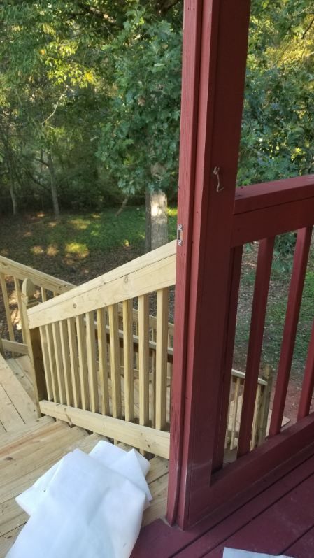 Wooden stairs with railing, leading to a deck with red trim, surrounded by trees.