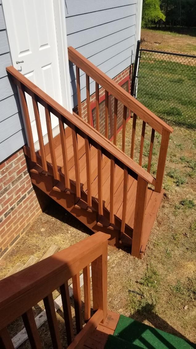 Wooden outdoor stairs with handrails against a blue house with a brick foundation.