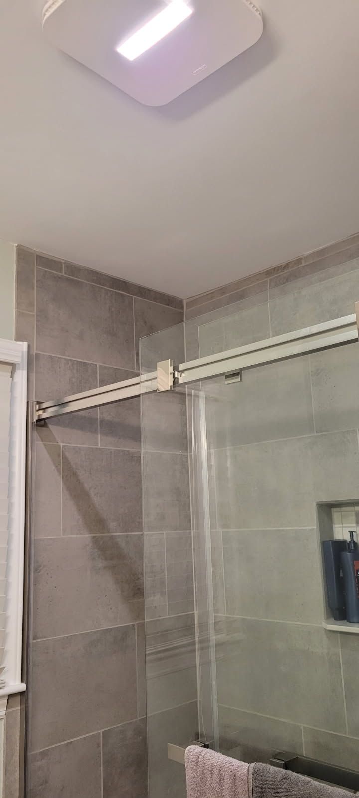 A bathroom corner with gray tile walls and a glass shower door.
