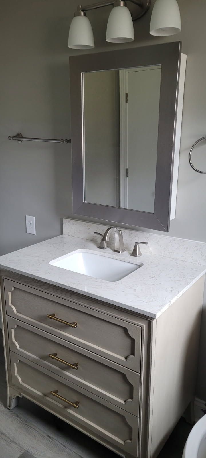 Bathroom vanity with white countertop, gray drawers, and framed mirror. Three light fixtures above.