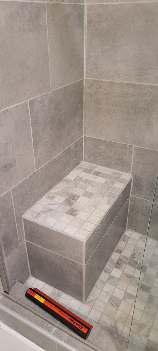 A tiled shower with a built-in seat. A red and yellow tool sits on the floor.