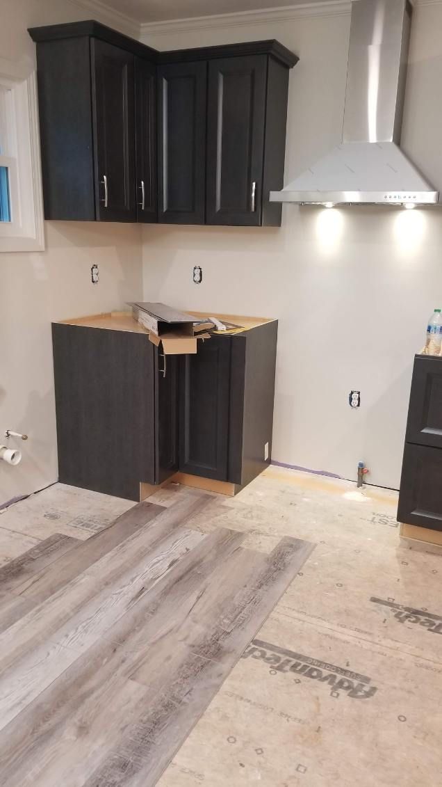Kitchen with dark gray cabinets, range hood, and wood-look flooring under construction.