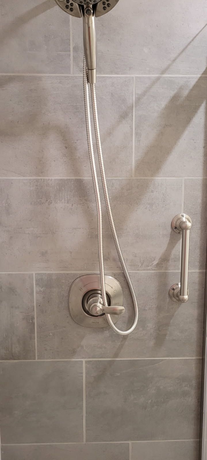 Shower with gray tiled wall, handheld shower head, and silver fixtures.