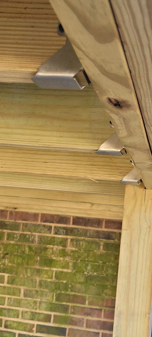 Wooden deck with metal brackets attached to brick wall.