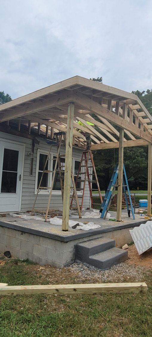 Construction of a porch roof on a small, weathered house. Ladders and materials are present.