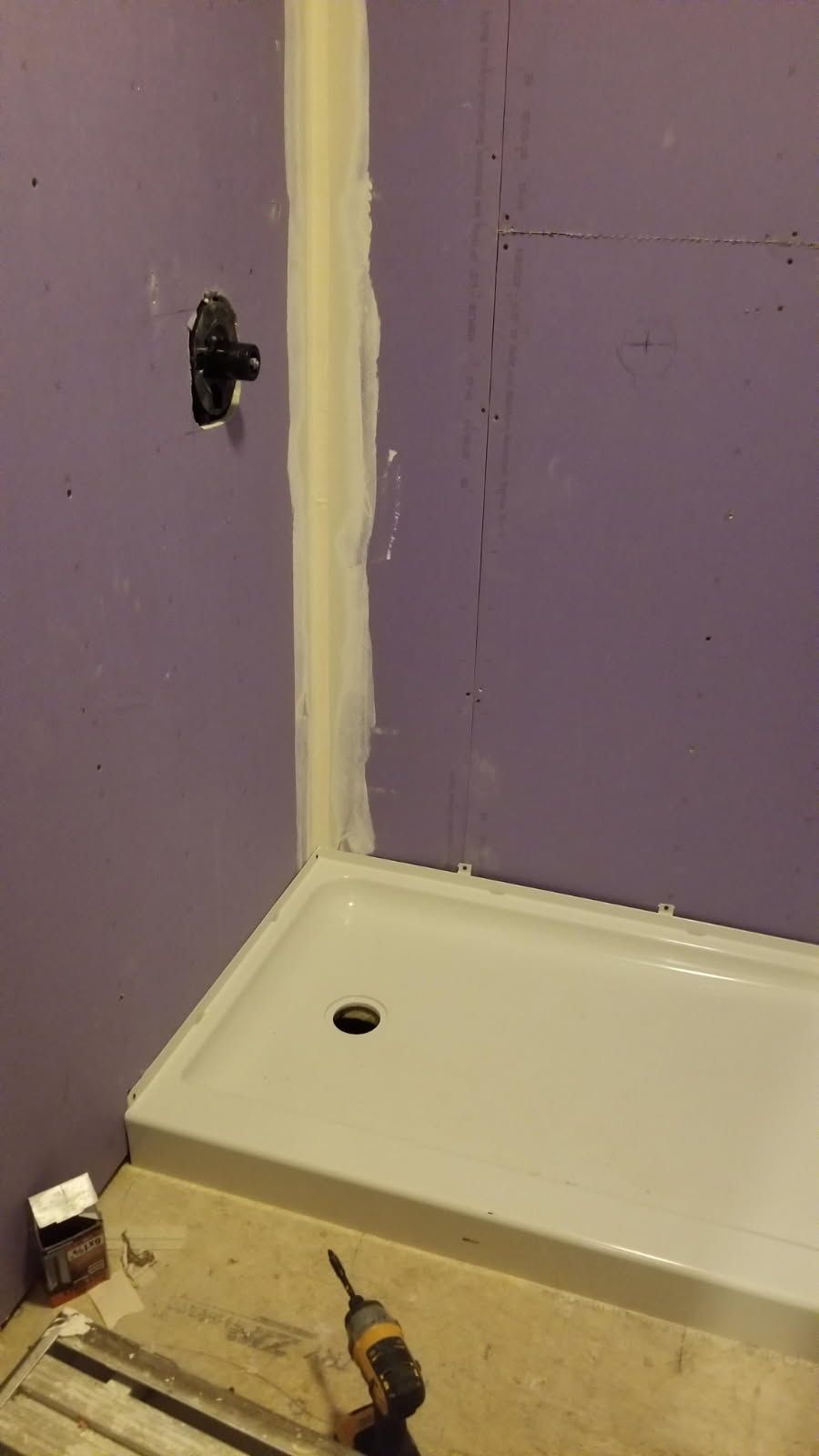 Shower stall renovation with purple wall, white shower base, and construction tools.
