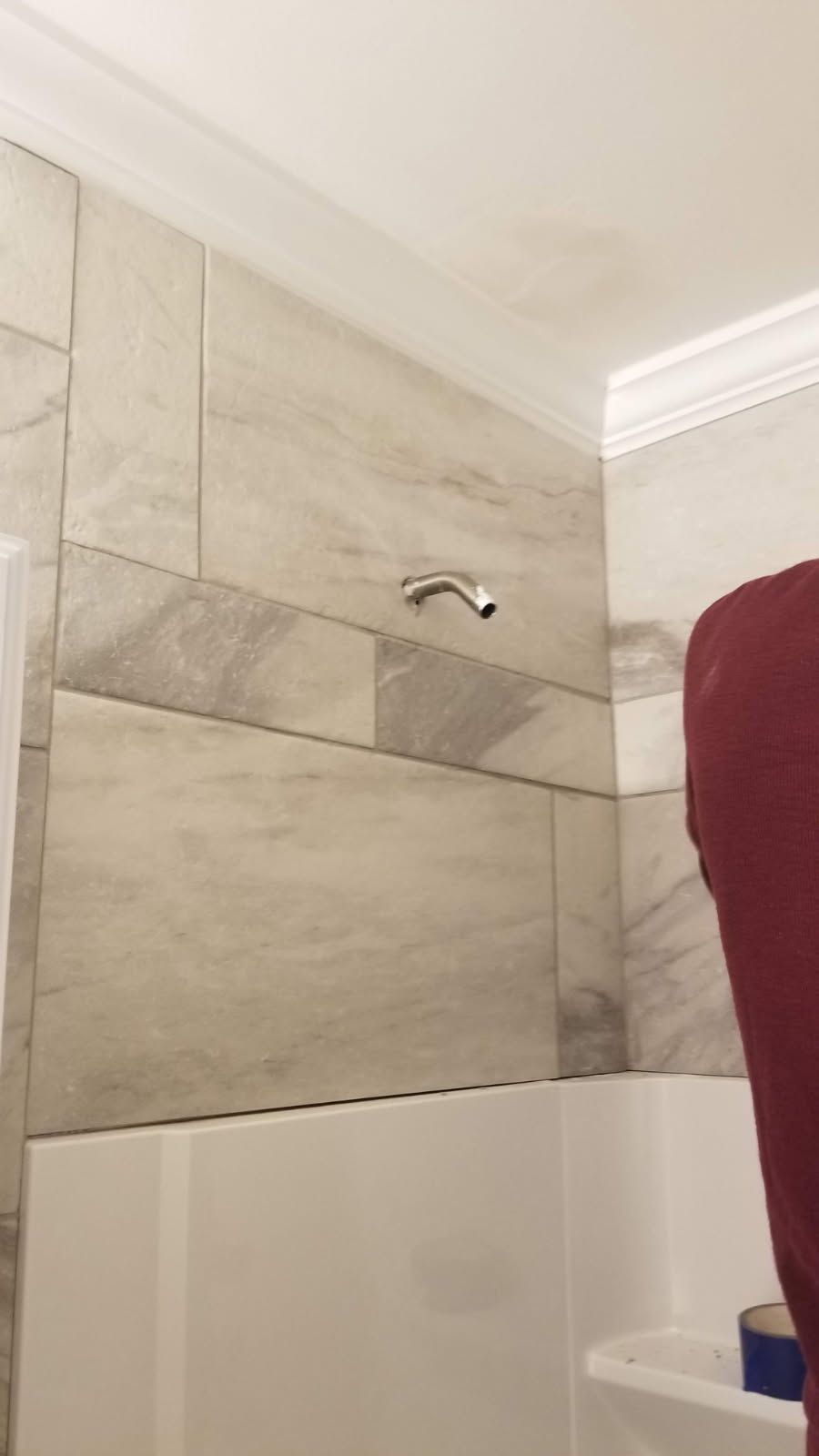 Shower with tiled walls, shower head, and white tub. A person in red is partially visible.