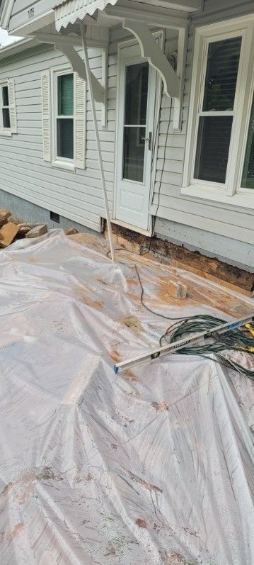 Exterior view of a house undergoing renovations. White siding, a door, windows, and a protective tarp.