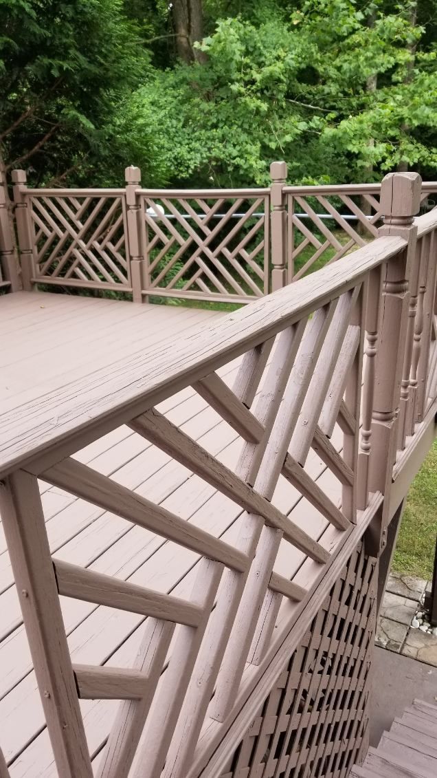 Beige deck with intricate lattice railing, overlooking a wooded area.