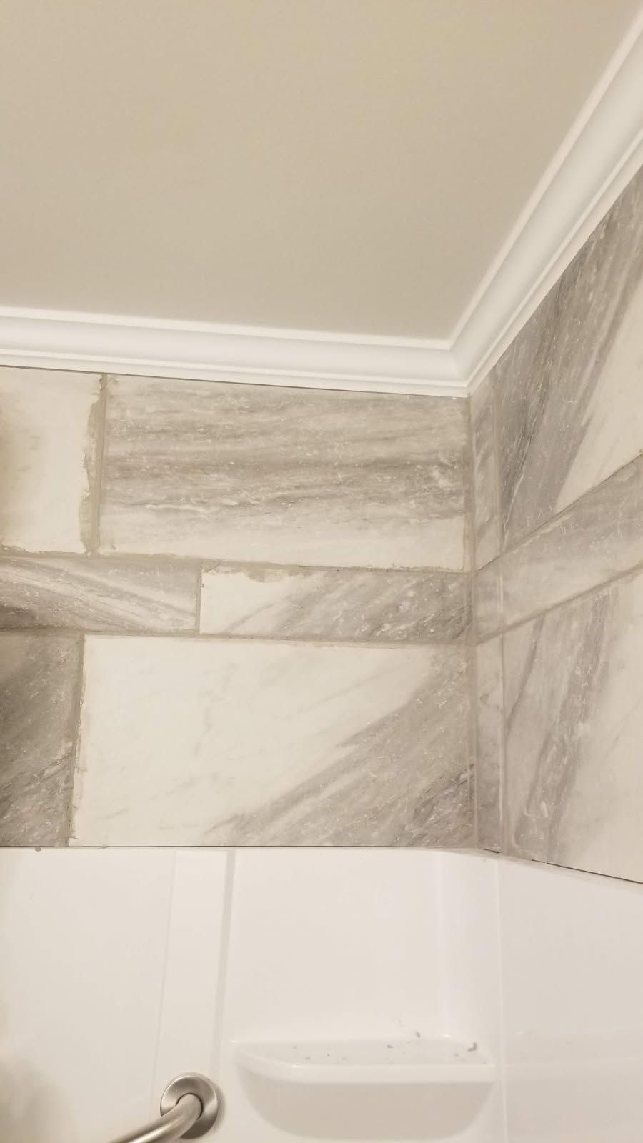 Bathroom corner with marble-patterned tile, white crown molding, and a built-in soap dish.