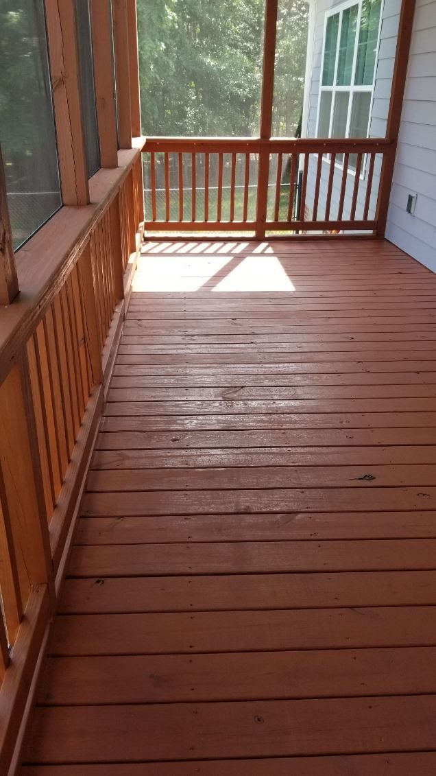 Wooden porch with distressed, brown painted floor and railings; sunlight.