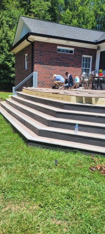 Brick building with patio steps being constructed. Men work on patio near the building. Green grass surrounds.