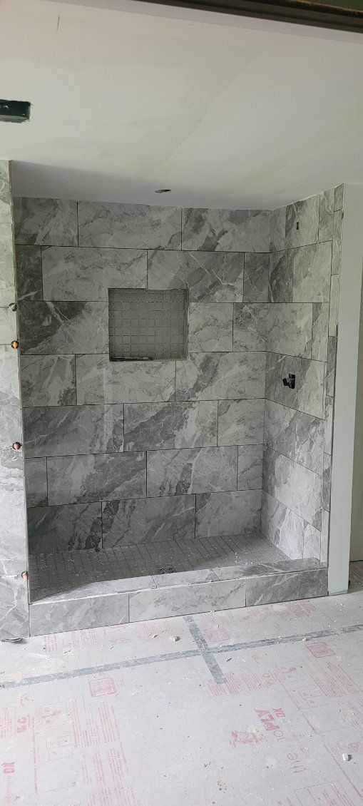 Stone wall under construction with a rectangular opening, in a room with white walls and a light-colored floor.