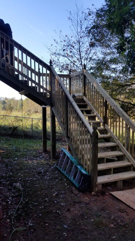 Wooden staircase structure leading up to a platform in a yard setting; blue ladder leaning against stairs.