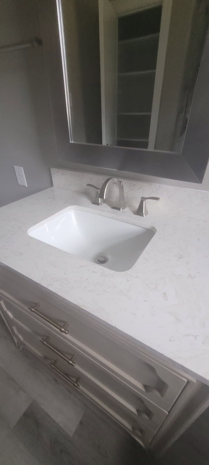 Bathroom sink with faucet and mirror. The countertop is white with grey cabinets below.