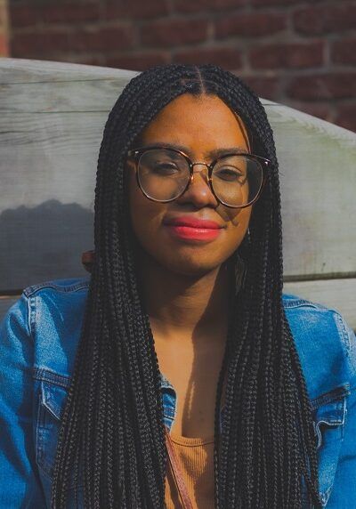 A woman with braids and glasses is sitting on a bench.