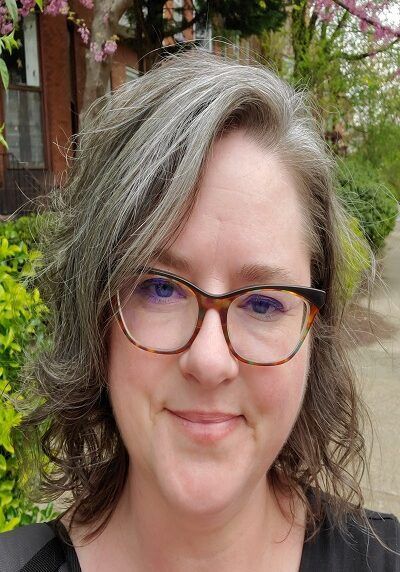 A woman with glasses and gray hair is smiling for the camera.