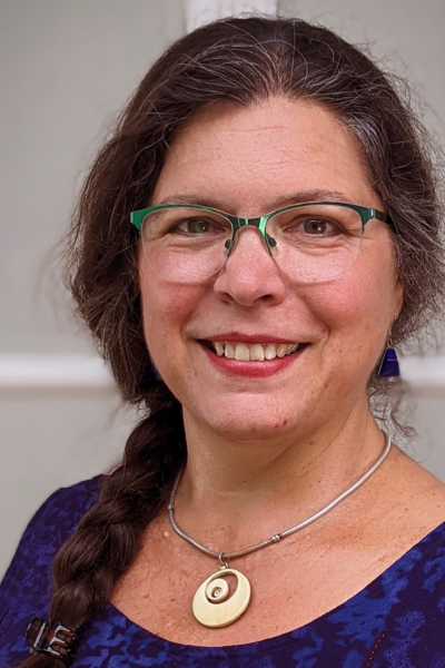A woman wearing glasses and a necklace is smiling for the camera.