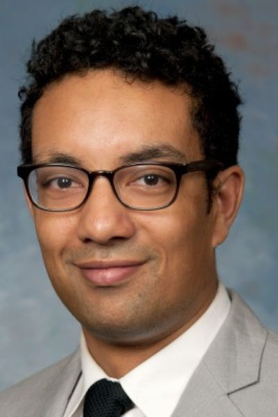 A man wearing glasses and a suit smiles for the camera