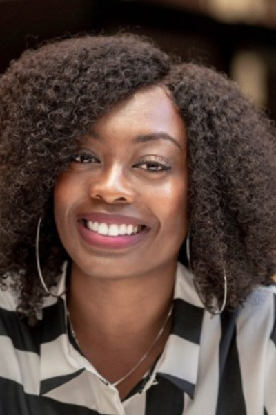 A woman with curly hair is wearing a black and white striped shirt and smiling.