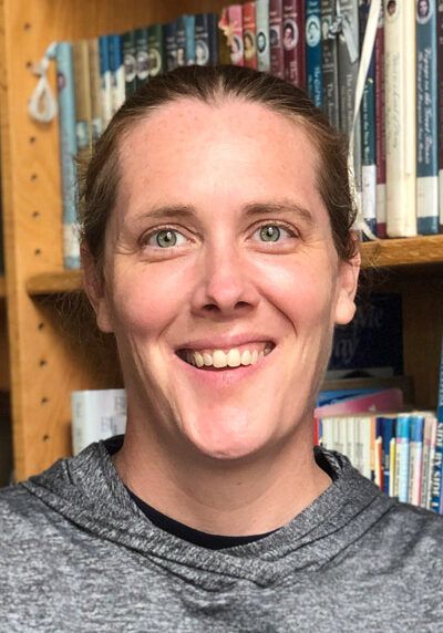 A woman is smiling in front of a bookshelf with books on it