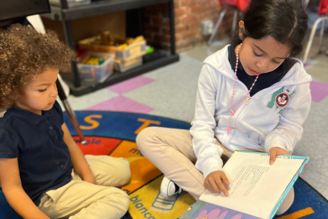 A boy and a girl are sitting on the floor reading books.