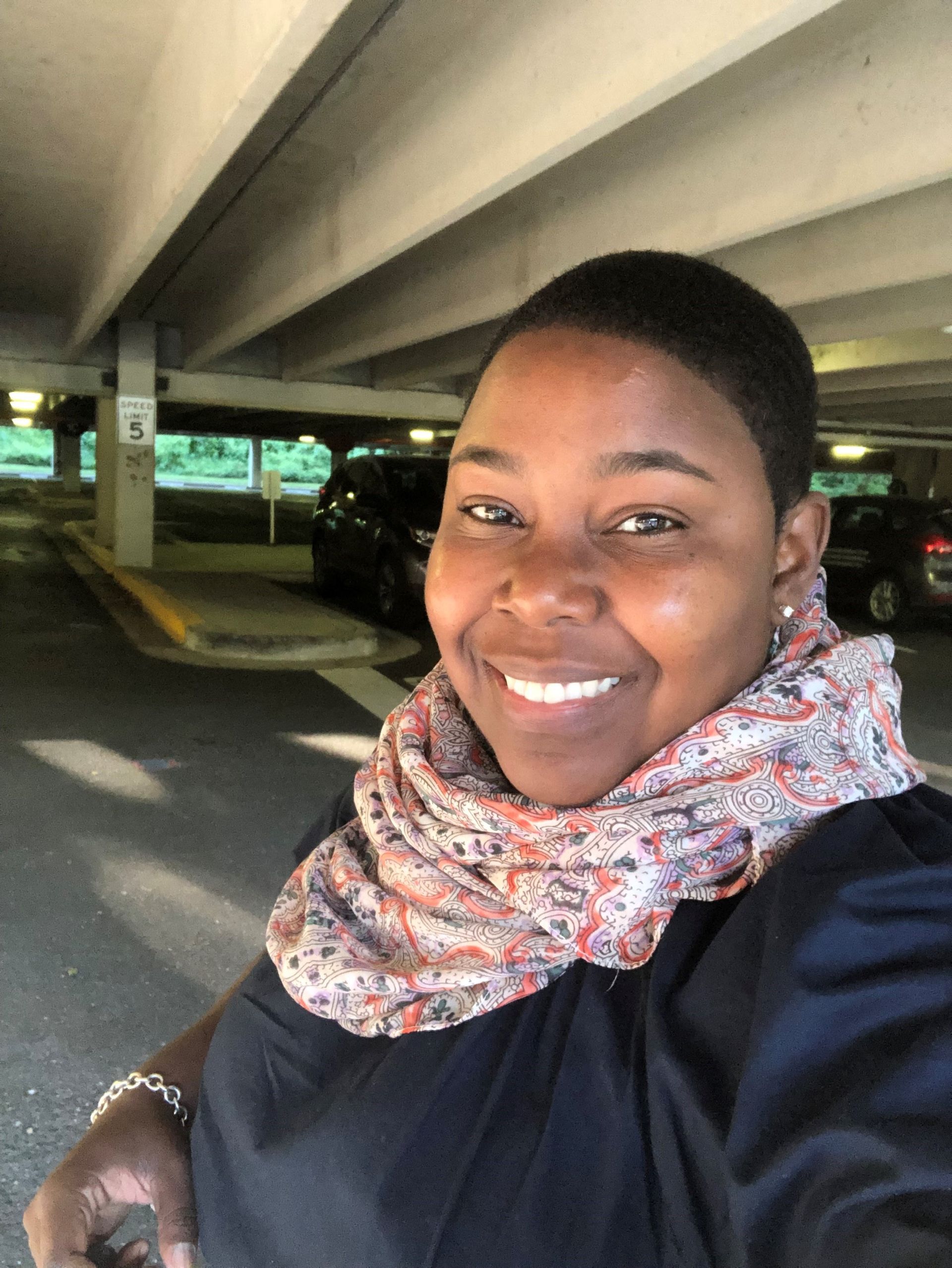 A woman wearing a scarf is taking a selfie in a parking garage.