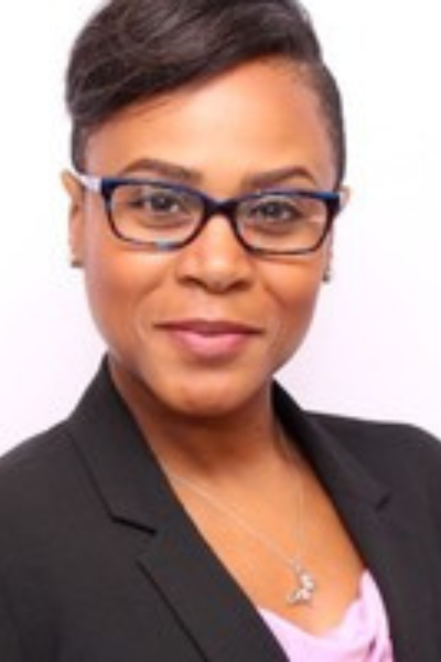 A woman wearing glasses and a black jacket is smiling for the camera.