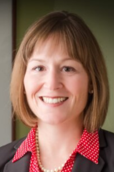 A woman wearing a red polka dot shirt and a black jacket smiles for the camera