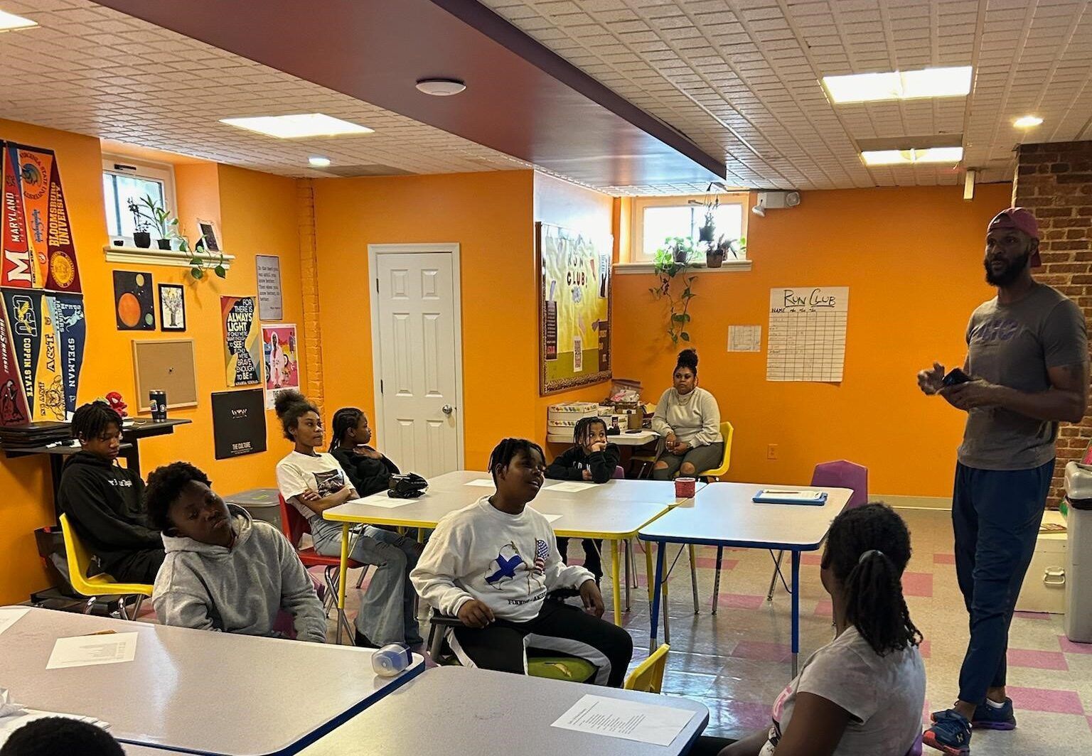 A group of people are sitting at tables in a room with orange walls.