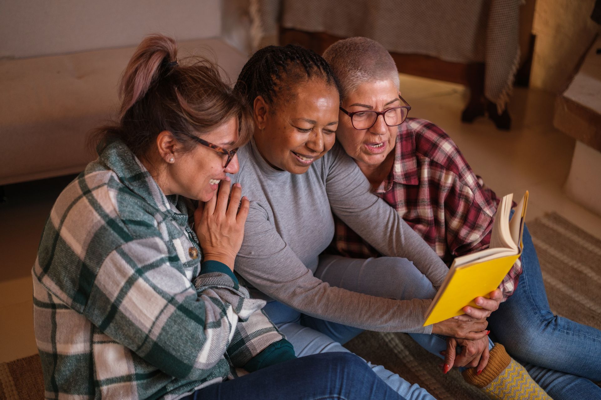 Three women are sitting on the floor reading a book together.