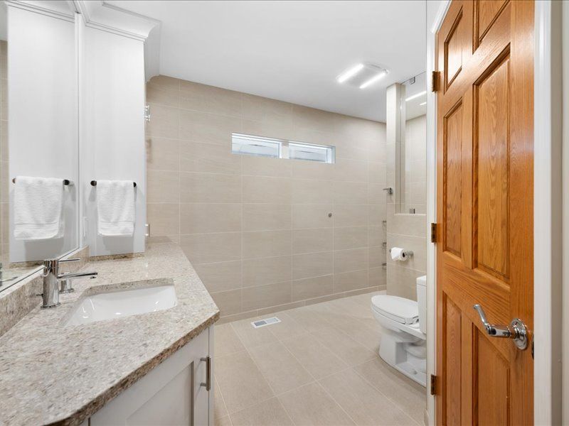 Bright bathroom with vanity, shower, toilet, and open wooden door