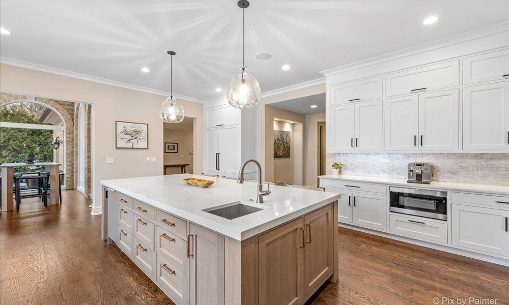 Warm kitchen with dark wood cabinets, island, and dining area, featuring polished hardwood floors and large windows