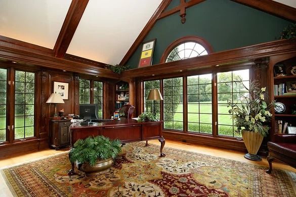 Sunlit living room with wood beams, large windows, rug, desk, and potted plants