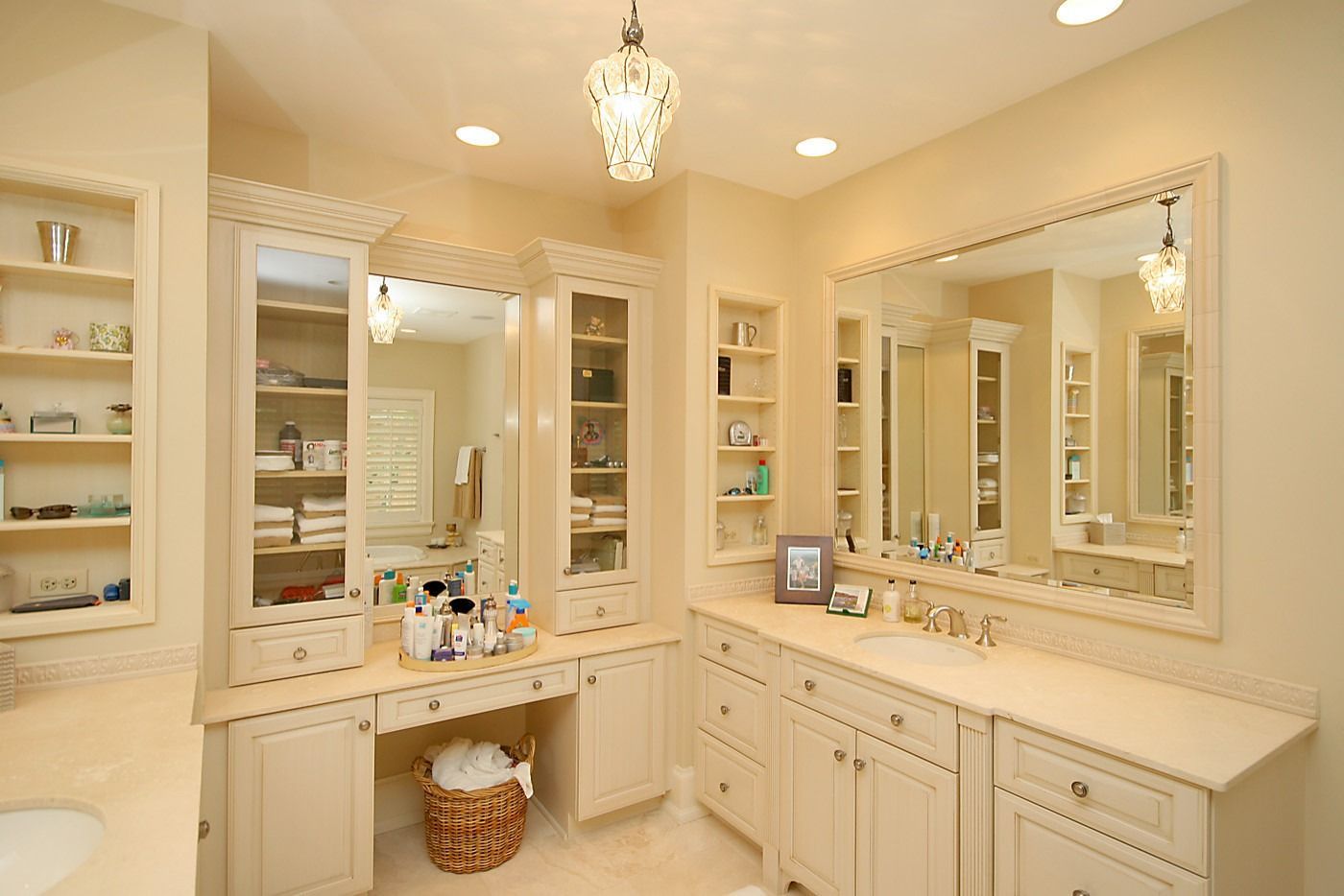 Bright beige bathroom with double sinks, large mirrors, vanity cabinets, and a chandelier.