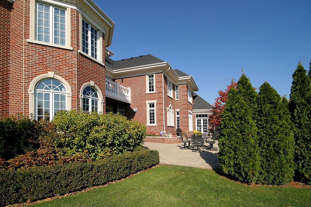 Brick suburban houses with manicured lawn, shrubs, and a walkway under a clear blue sky