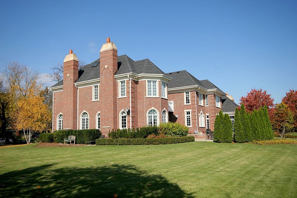 Large brick house with a dark roof on a grassy lawn under a clear blue sky