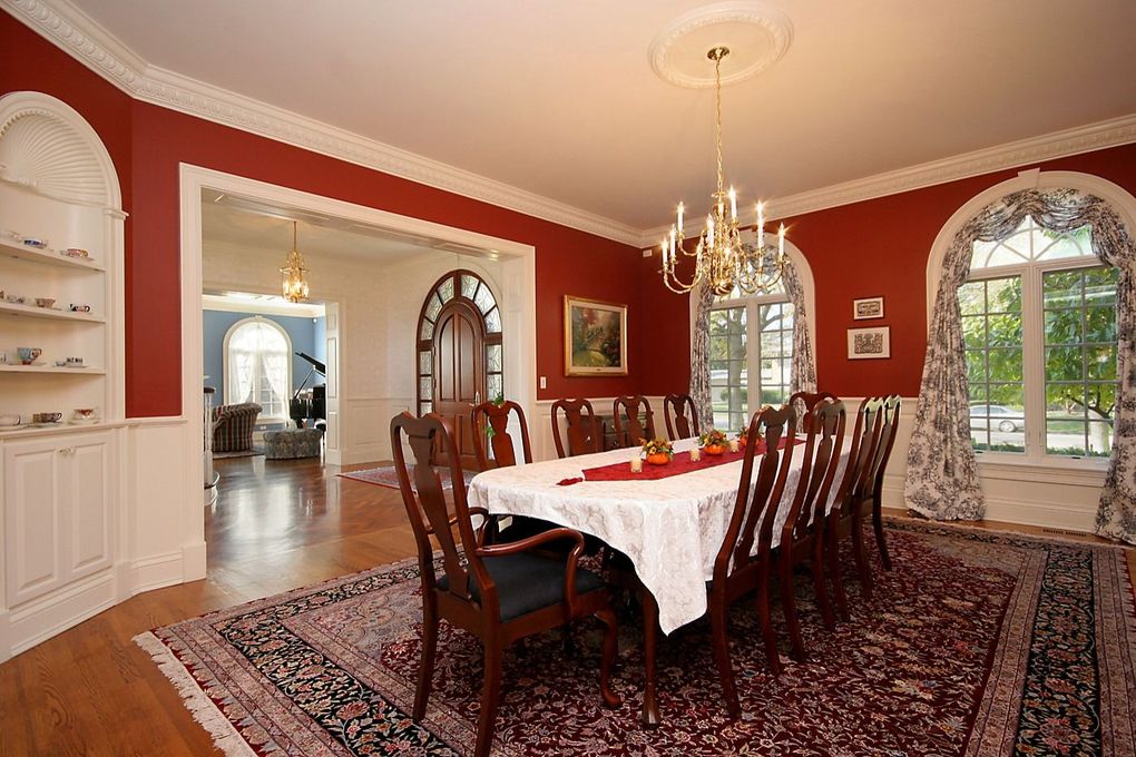 Elegant dining room with red walls, a long table, chandelier, patterned rug, and arched windows
