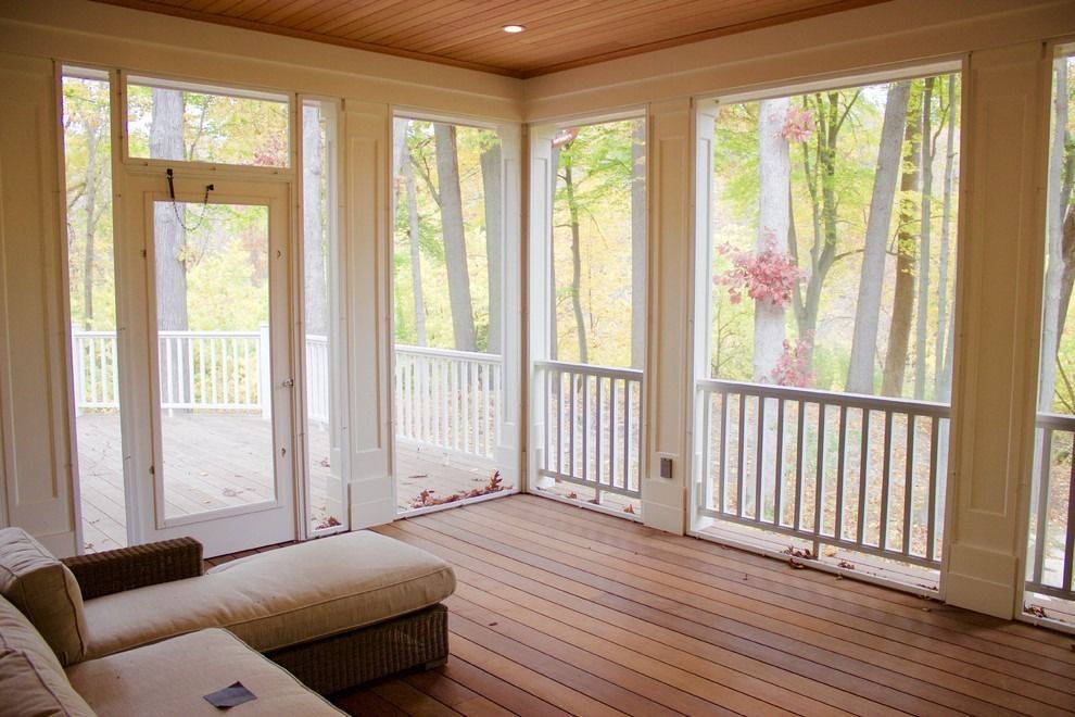 Bright sunroom with large windows, wood floor, and a patio door overlooking trees and a deck