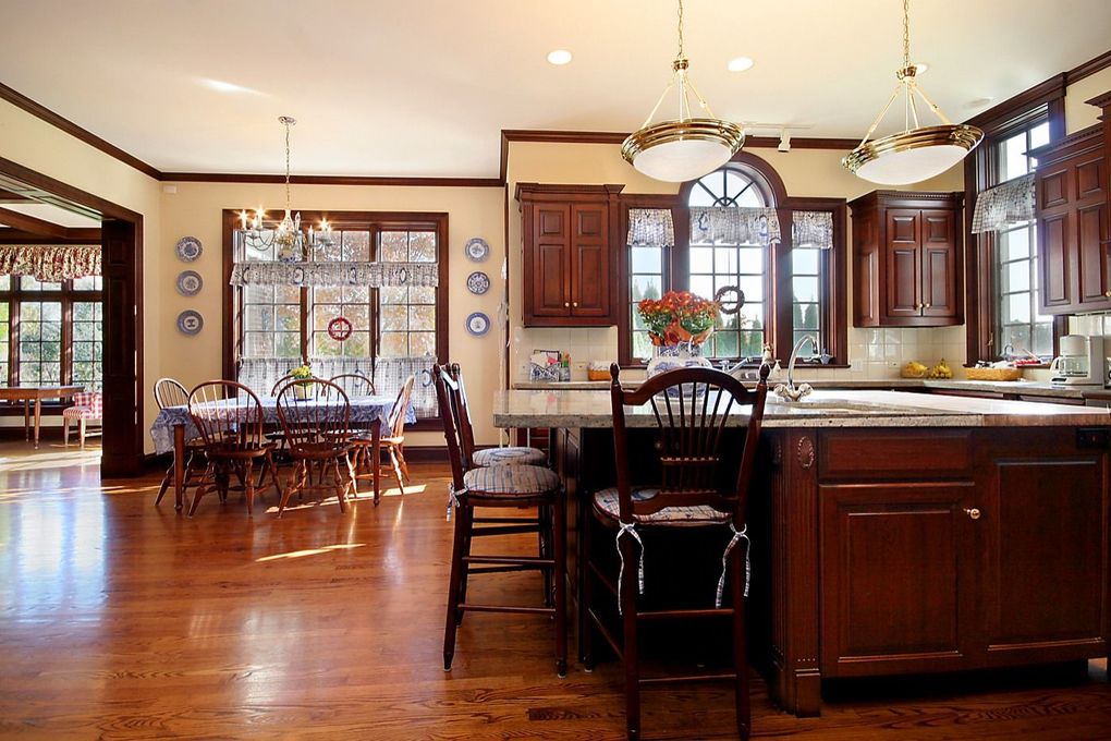 Warm kitchen with dark wood cabinets, island, and dining area, featuring polished hardwood floors and large windows