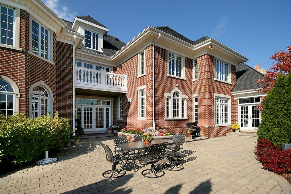 Brick mansion courtyard with outdoor tables, white-trimmed windows, and a sunny paved patio