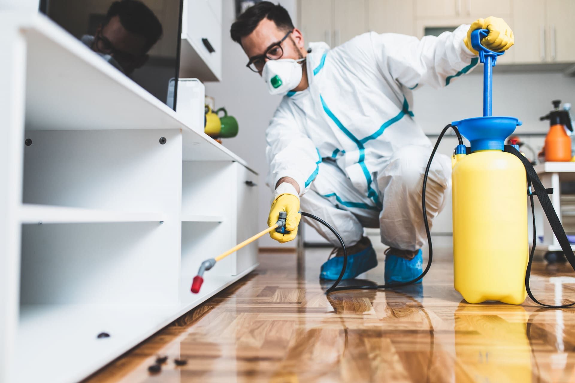 A Man In A Protective Suit Is Spraying Insecticide On A Wooden Floor — Caban's Pest Control In Lismore, NSW