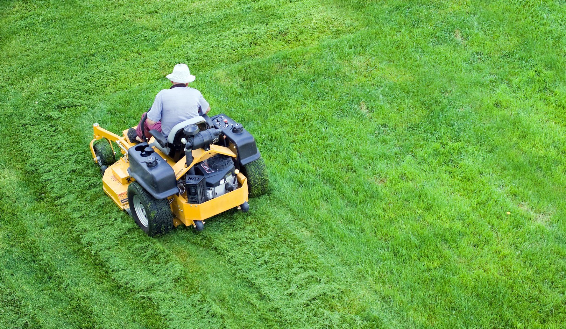 A man is riding a yellow lawn mower on a lush green lawn.